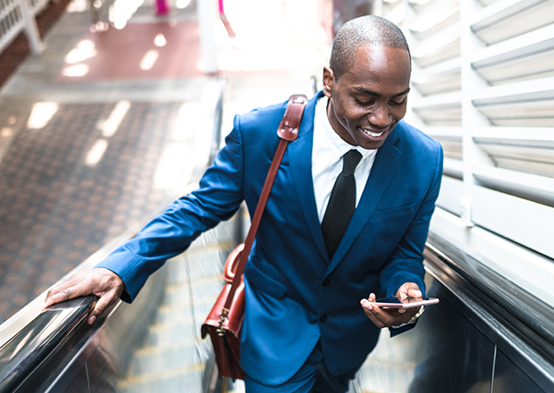 Man riding up escalator, holding a mobile phone